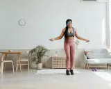 Mujer joven con auriculares realiza ejercicio hit saltando la cuerda en su sala de estar.