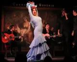 Una bailaora deslumbra con su traje azul, rodeada de guitarristas y cantantes, en una actuación que evoca a las mejores bailaoras de flamenco actuales.