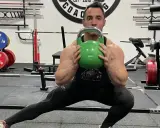 Hombre realiza desplantes laterales con pesa rusa verde en un gimnasio.