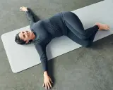 Mujer sonriente practicando ejercicios de yoga para relajarse, en posición de torsión acostada.