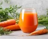 Un vaso de jugo de zanahoria fresco junto a zanahorias enteras. Descubre para qué es buena la zanahoria: ¡salud y vitalidad!