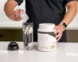 Hombre prepara batido con proteína en polvo para ganar músculo. El envase indica para qué sirve la proteína en polvo: energizar y recuperación post-entreno.