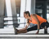 Mujer haciendo calentamiento antes de correr, estirando la pierna izquierda en un entorno urbano.