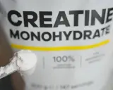 Bolsa de creatina monohidrato con una cuchara llena de polvo blanco. Ideal para potenciar tus músculos.
