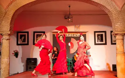 Tres bailarinas de flamenco, vestidas de rojo y con abanicos, ejecutan fandangos flamencos en un escenario.