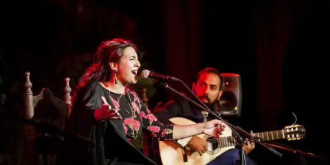 Cantante de flamenco actual, con vestido floral, canta apasionadamente mientras un guitarrista la acompaña.
