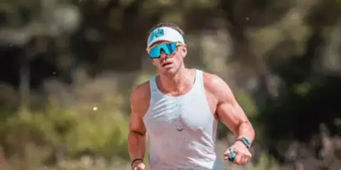 Atleta con gafas deportivas y visera, concentrado en como correr por un sendero.