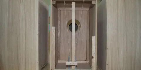 Partes de un cajón de madera, mostrando la estructura interna con cuerdas y un agujero circular.