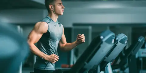 Joven con audífonos haciendo liss cardio en una cinta de correr en el gimnasio.