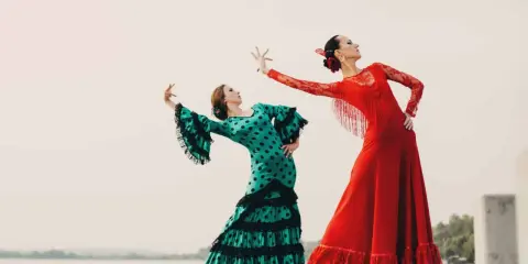 Dos bailarinas de flamenco, una con vestido verde de lunares y otra con rojo vibrante, ejecutan un apasionado flamenco ballo.