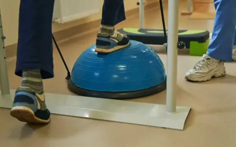 Persona practica ejercicios de equilibrio sobre una pelota azul, una forma de como regular el sistema nervioso y mejorar la coordinación.
