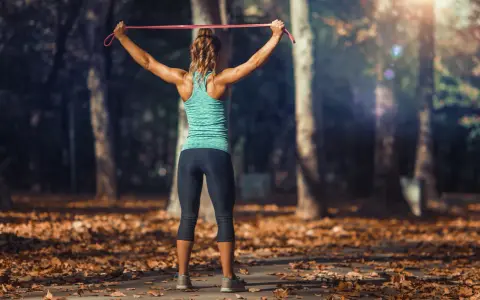 Mujer entrenando tren superior con tabla de ejercicios y gomas elásticas en un parque otoñal.