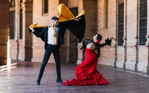 Pareja bailando flamenco con pasión. Él, con capa negra y dorada, ella, con vestido rojo voluminoso. Un jaleo flamenco lleno de arte.