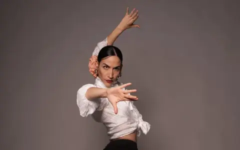 Bailarina de flamenco con flor en el pelo, ejecutando elegantes pasos de flamenco con expresión intensa.