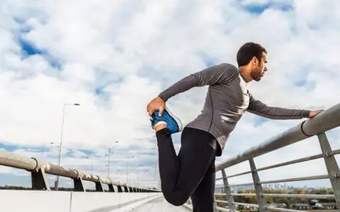 Hombre haciendo estiramientos antes de correr en un puente, con el cielo nublado de fondo.