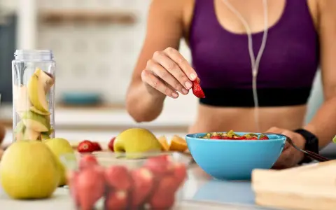 Mujer en ropa deportiva prepara su desayuno saludable con frutas frescas, pensando en qué desayunar antes de entrenar.