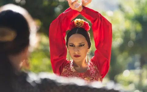Mujer con traje rojo de flamenca, brazos en alto, mirando a otra persona.