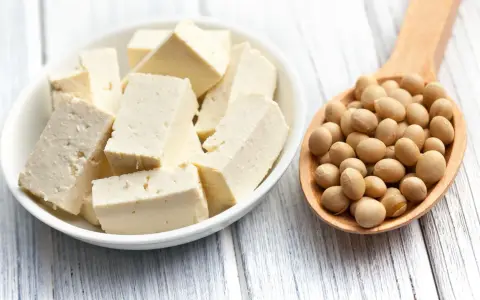 Tofu cortado en cubos en un bol blanco y una cuchara de madera llena de semillas de soja. ¿A qué sabe el tofu?