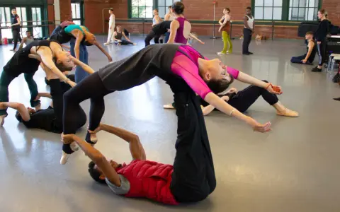 Un grupo de bailarines practica una coreografía compleja, con un hombre en el suelo sosteniendo a una mujer en el aire, evocando la pasión de un flamenco.
