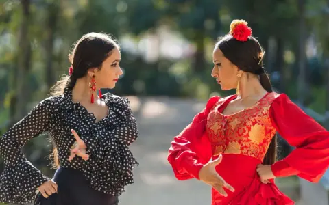 Dos mujeres practican baile flamenco para principiantes en un parque, una con traje de lunares y otra de rojo vibrante.