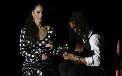 Una bailaora flamenca con vestido de lunares y un guitarrista crean un duende que es pura pasión en la oscuridad.