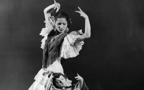 Una bailarina española famosa, con volantes y mantón, baila con gracia mientras una niña yace a sus pies.