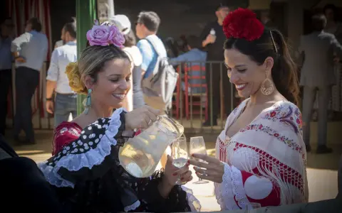 Dos mujeres con trajes de flamenca, una sirviendo bebida. Un vistazo a la historia del traje de flamenca.