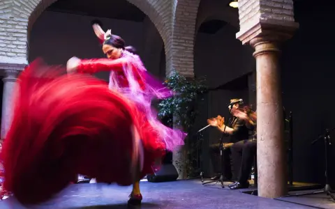 Una bailaora española gira con su vestido rojo, creando un torbellino de tela. A su lado, un guitarrista acompaña con su música.