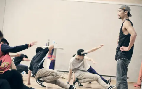 Jóvenes practicando una coreografía de break dance, con movimientos en el suelo y un instructor observando.