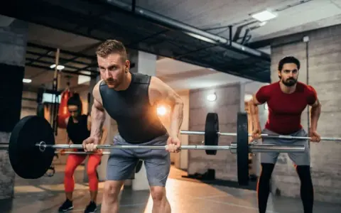 Hombres y mujeres realizando ejercicios de espalda en el gym con barras.
