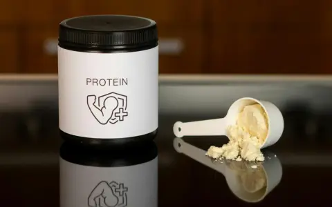 Un bote de proteína y una cuchara con polvo. Ideal para saber como tomar proteína y potenciar tus entrenamientos.