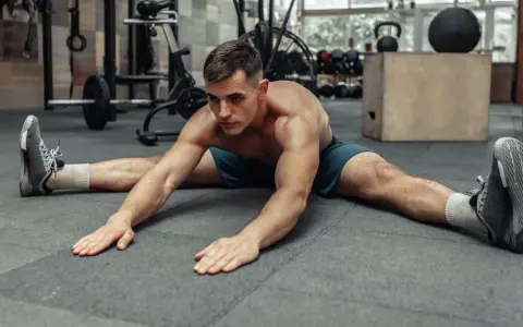 Hombre haciendo estiramiento de piernas en el suelo, preparándose para el calentamiento antes de entrenar.