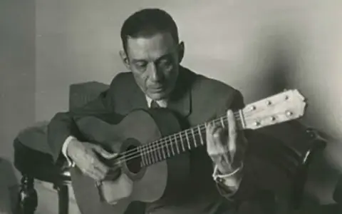 Un guitarrista flamenco andaluz, con traje y corbata, toca su guitarra con pasión.