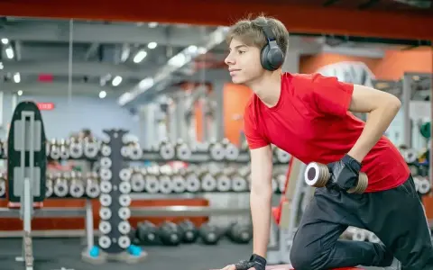 Joven con auriculares entrena en gimnasio. ¿Hacer pesas a los 15 años detiene mi crecimiento?