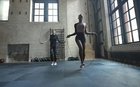 Dos mujeres realizan ejercicios de calentamiento general saltando la cuerda en un gimnasio industrial.