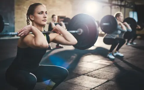 Mujeres realizando sentadillas con barra, un ejemplo de ejercicios compuestos en el gym.