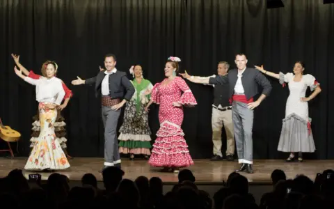 Artistas de sevillanas y flamenco en escena, con trajes coloridos y movimientos apasionados.