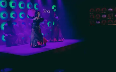 Dos bailarinas de danza sevillana, con trajes vibrantes, actúan bajo luces púrpuras y verdes.