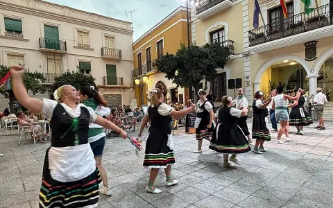 Un grupo de mujeres realiza un animado fandango dance en una plaza, vestidas con trajes tradicionales.