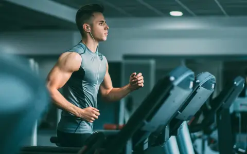 Joven con audífonos haciendo liss cardio en una cinta de correr en el gimnasio.