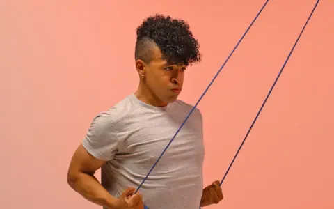 Hombre con cabello rizado haciendo ejercicio con banda elástica para mejorar la movilidad tren superior.