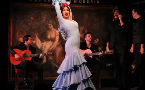 Una bailaora deslumbra con su traje azul, rodeada de guitarristas y cantantes, en una actuación que evoca a las mejores bailaoras de flamenco actuales.