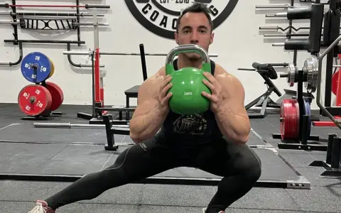 Hombre realiza desplantes laterales con pesa rusa verde en un gimnasio.