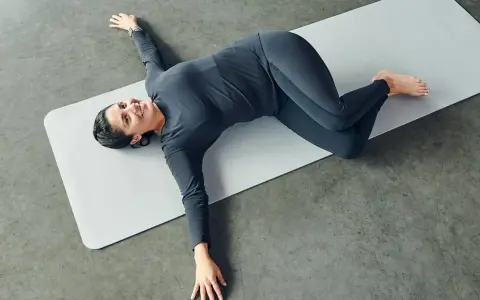 Mujer sonriente practicando ejercicios de yoga para relajarse, en posición de torsión acostada.