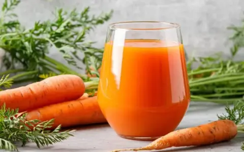 Un vaso de jugo de zanahoria fresco junto a zanahorias enteras. Descubre para qué es buena la zanahoria: ¡salud y vitalidad!