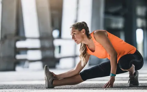 Mujer haciendo calentamiento antes de correr, estirando la pierna izquierda en un entorno urbano.