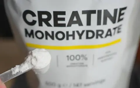 Bolsa de creatina monohidrato con una cuchara llena de polvo blanco. Ideal para potenciar tus músculos.