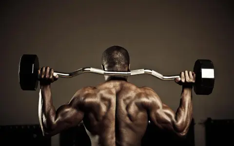 Hombre musculoso con barra detrás del cuello, trabajando para fortalecer lumbares.
