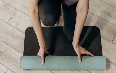 Manos enrollando una esterilla de yoga verde sobre una esterilla negra. Un paso esencial para saber como limpiar esterilla yoga y mantenerla en buen estado.