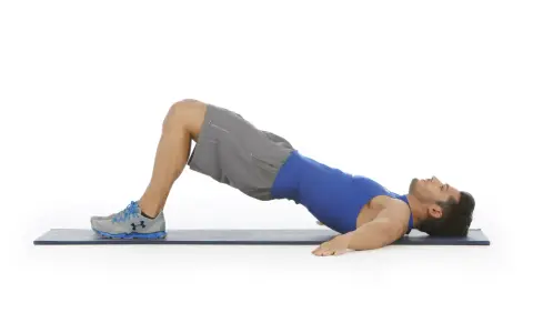 Hombre realizando puente de glúteo, un ejercicio clave para fortalecer la zona lumbar en el gym.